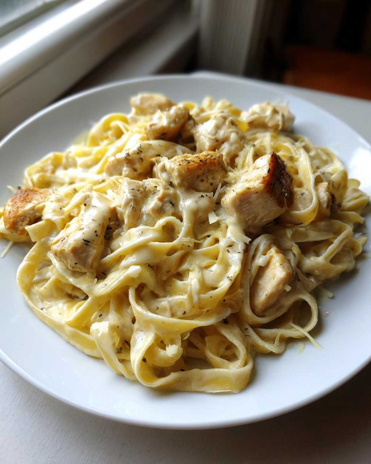 A close-up of creamy chicken pasta made with fettuccine noodles, topped with seared chicken pieces and grated Parmesan cheese.