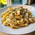 Close-up of creamy chicken pasta featuring fettuccine noodles coated in a rich sauce and topped with diced chicken and fresh parsley.