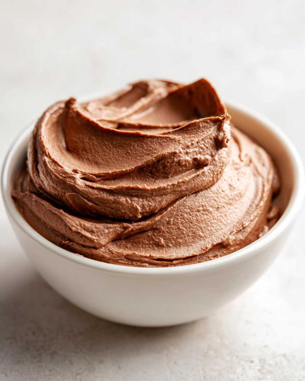 A close-up of rich, creamy chocolate dip swirled high in a small white bowl.