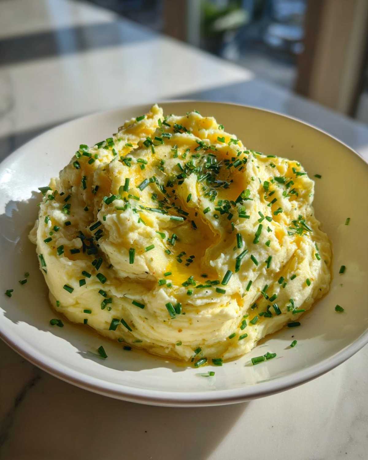 A creamy bowl of fluffy garlic mashed potatoes topped with melted butter and fresh chopped chives.