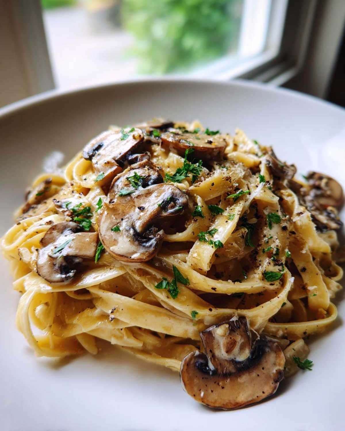 A close-up of creamy fettuccine mushroom pasta topped with sautéed mushrooms and fresh parsley.