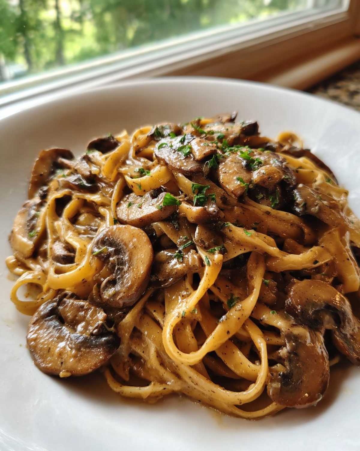 Close-up of a bowl of creamy mushroom pasta, featuring fettuccine noodles and sliced, sautéed mushrooms.