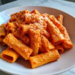 Close-up of rigatoni pasta coated in vibrant pink sauce pasta, topped with grated cheese.