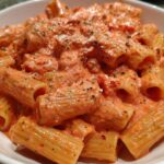Close-up of rigatoni pasta coated generously in a creamy, orange-hued pink sauce pasta, topped with herbs and grated cheese.