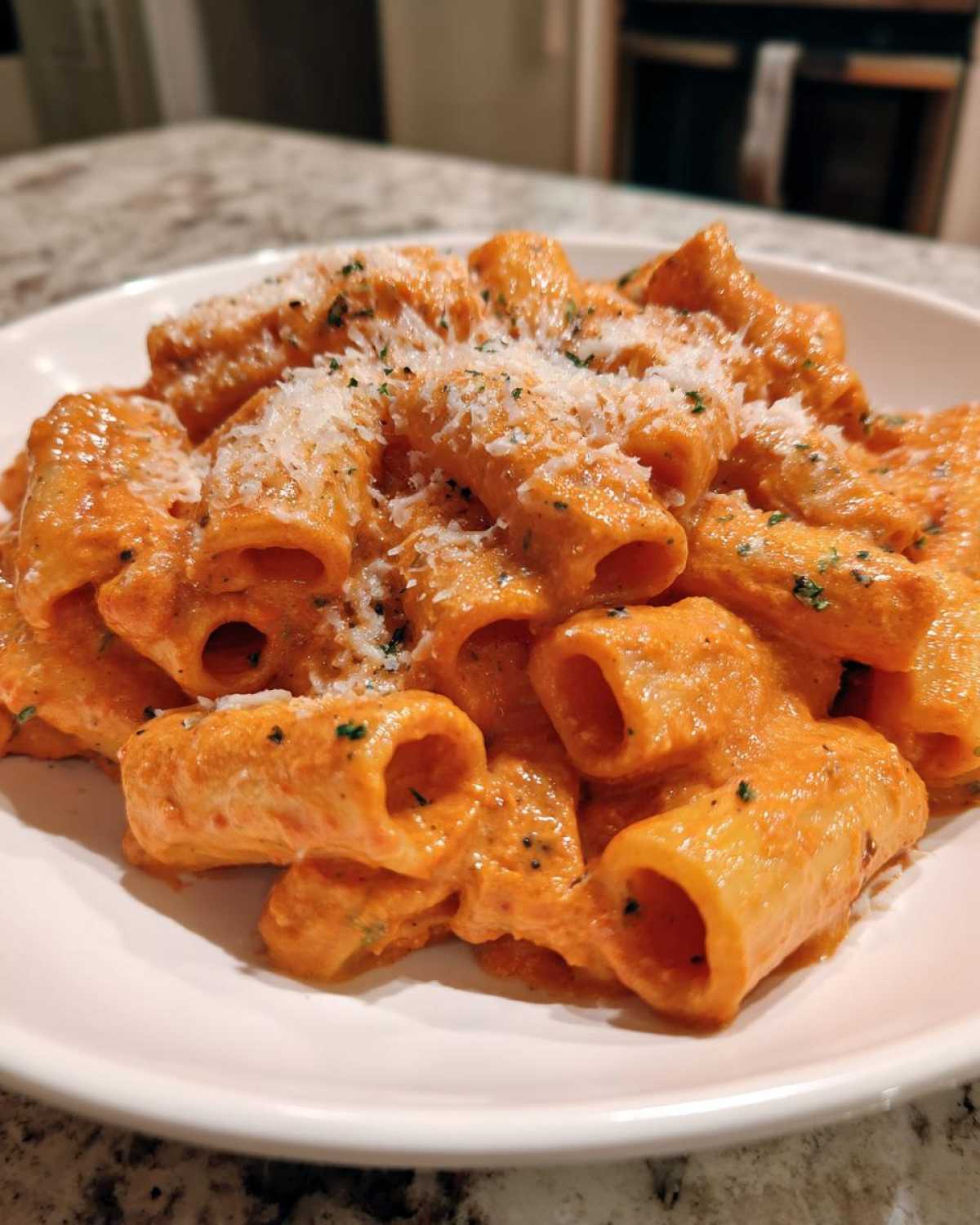 Close-up of rigatoni pasta coated in creamy pink sauce pasta, topped with grated Parmesan and herbs.