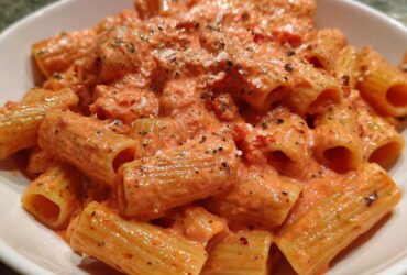 Close-up of rigatoni pasta coated generously in a creamy, orange-hued pink sauce pasta, topped with herbs and grated cheese.