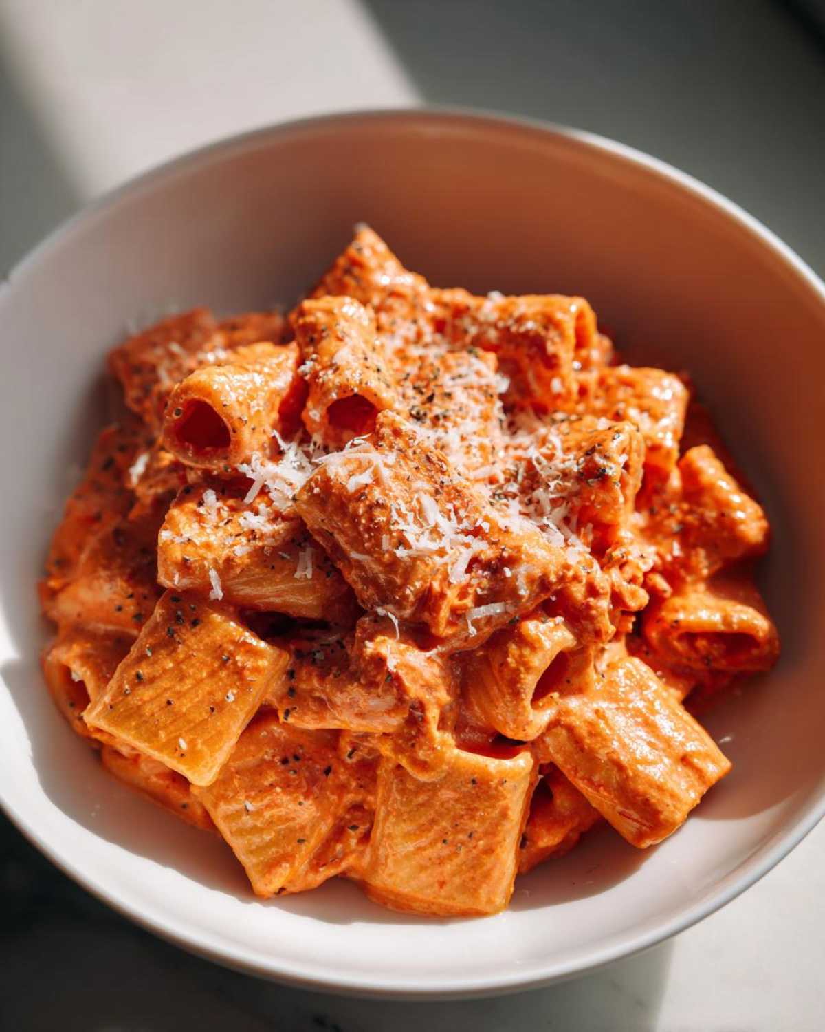 Close-up of rigatoni pasta coated in creamy, vibrant pink sauce pasta, topped with grated cheese and black pepper.