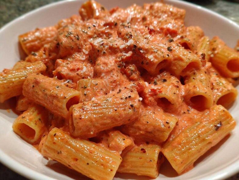 Close-up of rigatoni pasta coated generously in a creamy, orange-hued pink sauce pasta, topped with herbs and grated cheese.