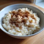 A close-up of a white bowl filled with creamy rice pudding recipe, generously sprinkled with cinnamon.