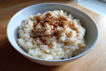 A close-up of a white bowl filled with creamy rice pudding recipe, generously sprinkled with cinnamon.