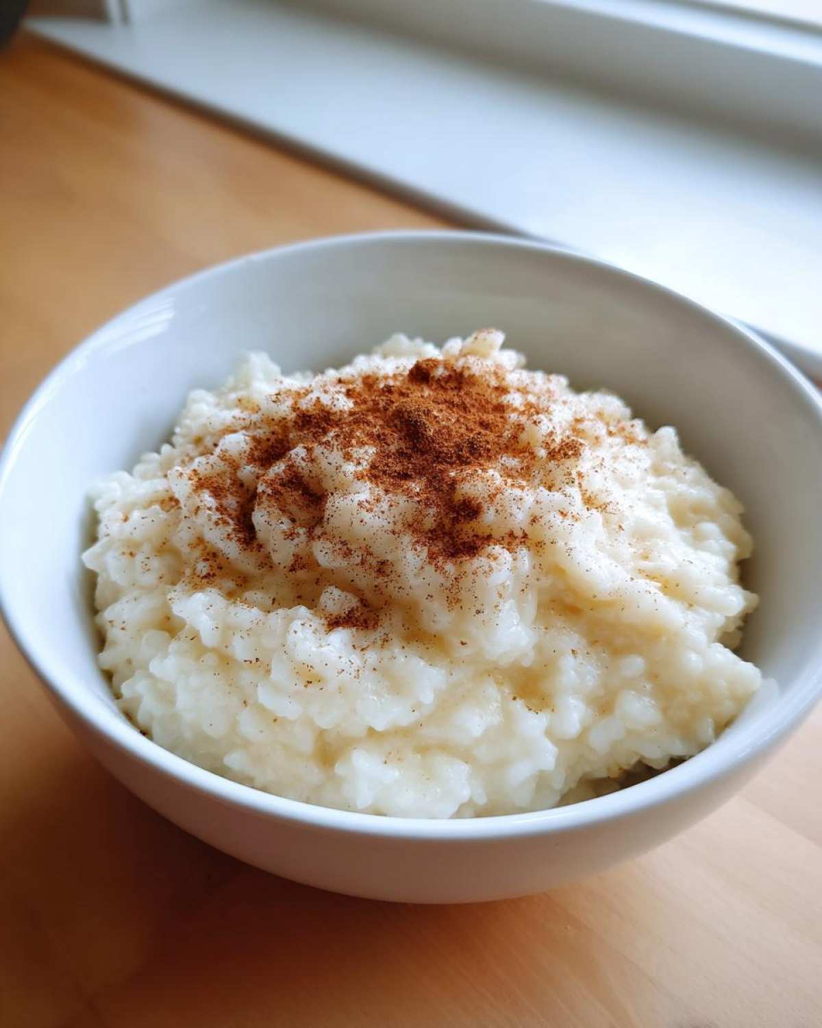 A close-up of creamy rice pudding recipe served in a white bowl, generously topped with ground cinnamon.