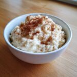 A close-up of a white bowl filled with creamy rice pudding recipe, generously sprinkled with ground cinnamon.