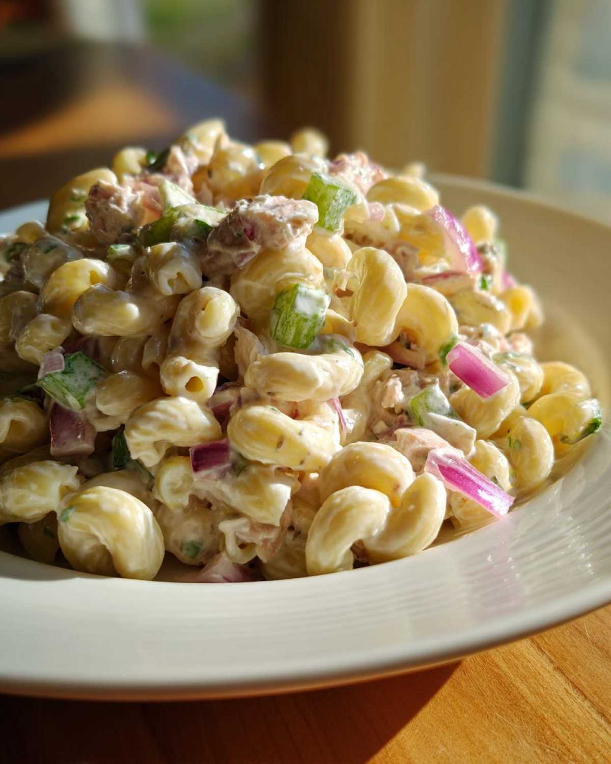 Close-up of creamy Tuna pasta salad featuring elbow macaroni, red onion, and celery in a white bowl.