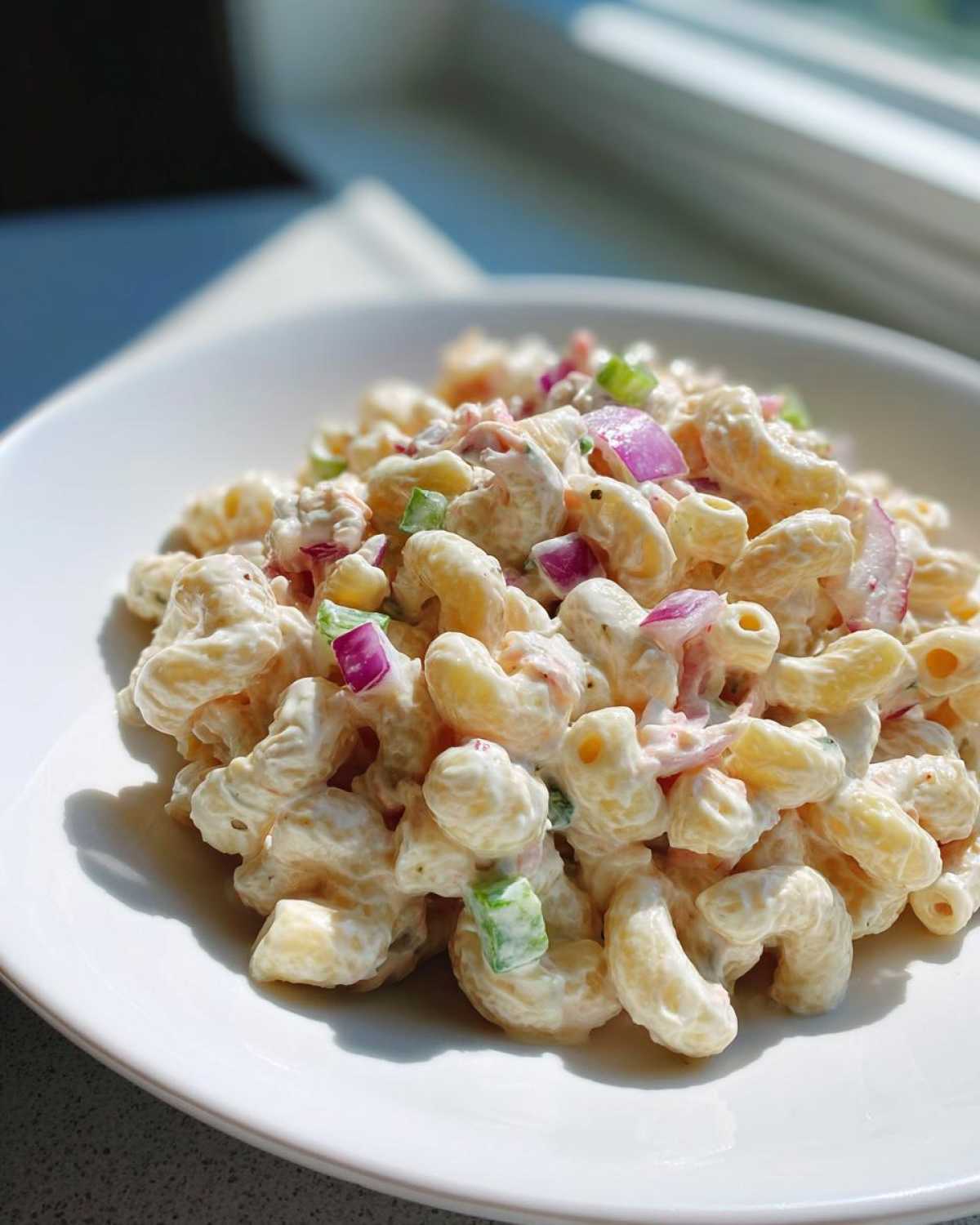 A close-up of creamy Tuna pasta salad featuring elbow macaroni, diced red onion, and green peppers served in a white bowl.