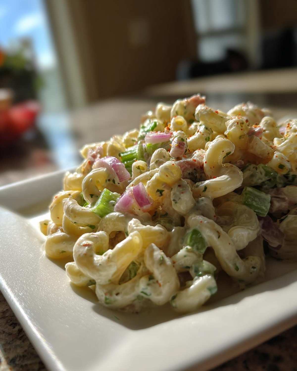 Close-up of creamy Tuna pasta salad featuring elbow macaroni, red onion, and celery, sprinkled with paprika.