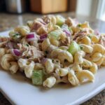 A close-up of a creamy serving of tuna pasta salad featuring elbow macaroni, flaked tuna, celery, and red onion.