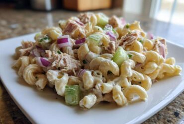 A close-up of a creamy serving of tuna pasta salad featuring elbow macaroni, flaked tuna, celery, and red onion.