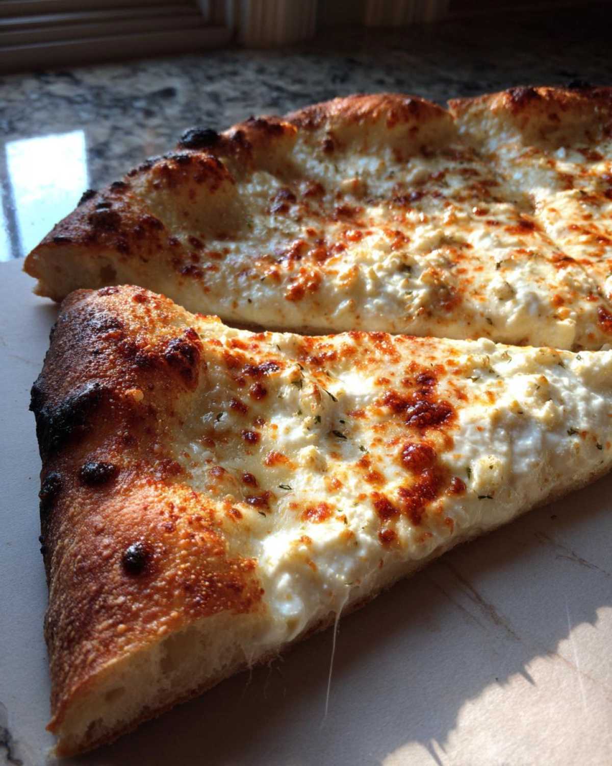 A close-up of a slice of amazing 10-minute creamy white pizza showing the thick, bubbly ricotta topping and charred crust.