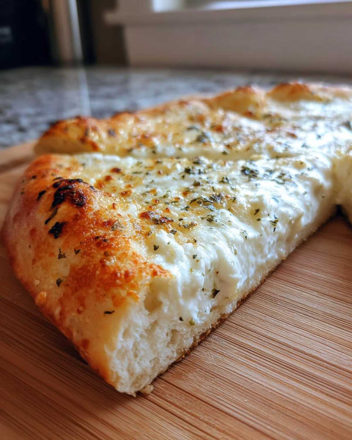 A thick slice of creamy white pizza showing the fluffy crust and generous layer of white cheese topping sprinkled with dried herbs.