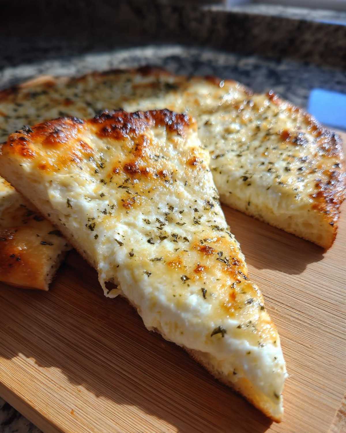 A thick slice of creamy white pizza topped with melted cheese and dried herbs, resting on a wooden board.