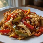 A close-up of shredded chicken mixed with colorful red and green bell pepper strips, ready to serve for crockpot chicken fajitas.
