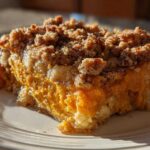 A close-up slice of rich, orange crockpot sweet potato casserole topped with a crunchy pecan streusel.