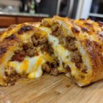 Close-up of a cross-section of baked garbage bread overflowing with melted cheese and seasoned ground meat.