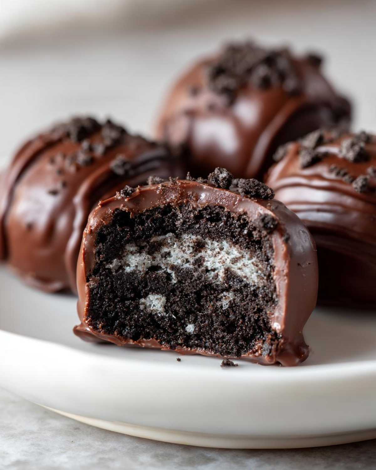 Close-up of a chocolate-dipped Oreo balls, one cut in half revealing the dark cookie filling and white cream center.