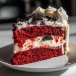 Close-up of a rich slice of red velvet cheesecake showing layers of bright red cake and white filling, topped with cream.