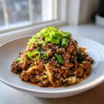 A close-up of a serving of egg roll in a bowl, featuring ground meat, cabbage, topped with sesame seeds and fresh green onions.