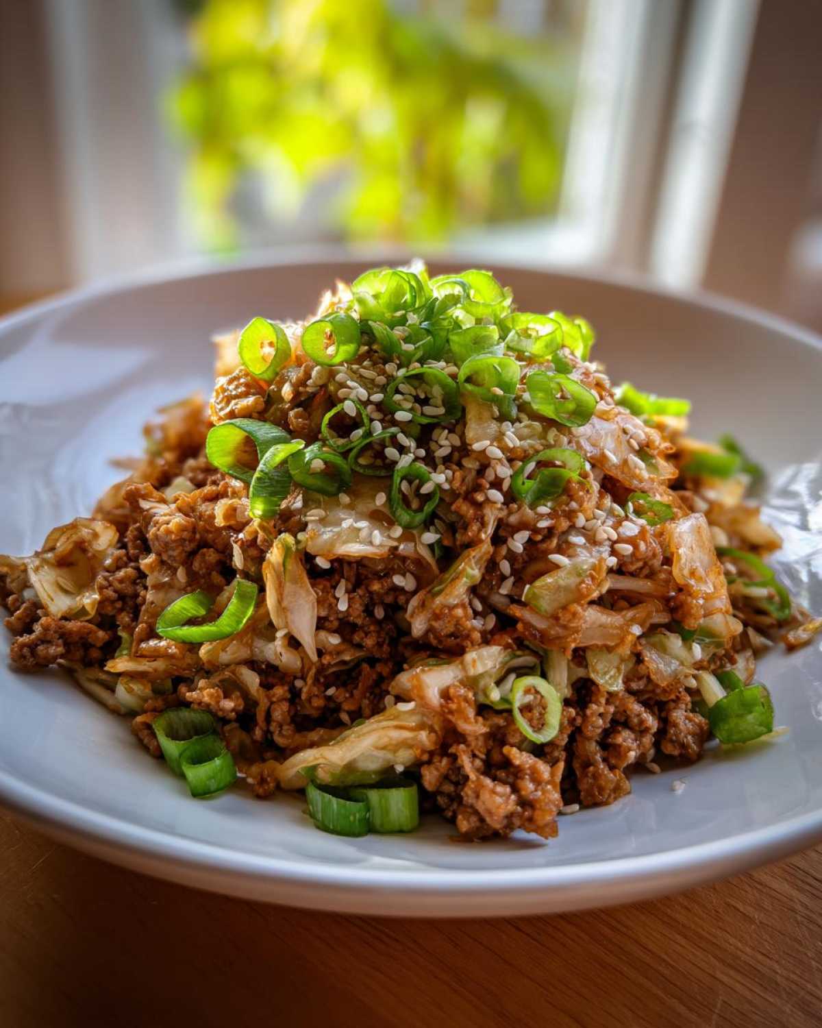 A close-up of a serving of egg roll in a bowl, featuring ground meat and cabbage, garnished with sesame seeds and fresh green onions.
