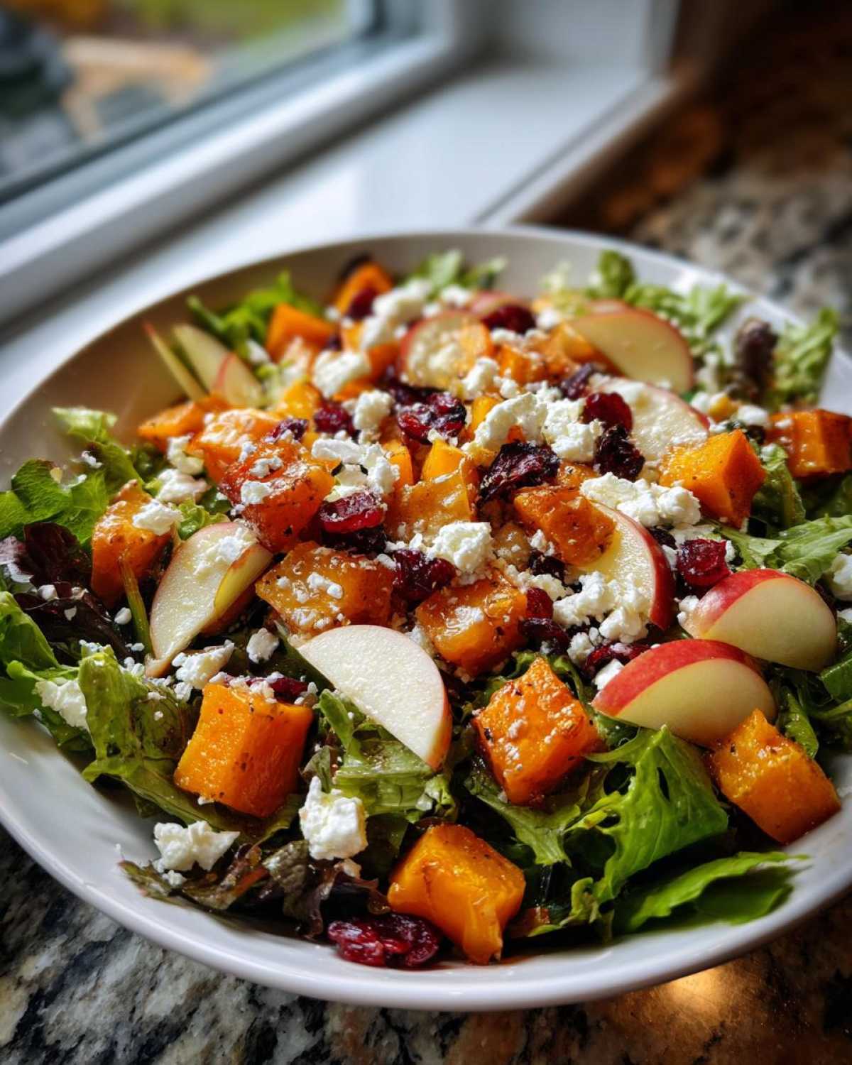 A vibrant bowl featuring a fall harvest salad with roasted squash, apple slices, cranberries, and feta cheese on mixed greens.