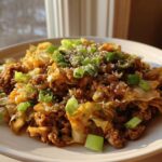 A close-up of a serving of egg roll in a bowl, featuring ground meat and cabbage topped with green onions and sesame seeds.