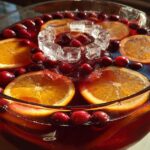 Close-up of a festive thanksgiving punch in a glass bowl, garnished with orange slices, whole cranberries, and ice cubes.