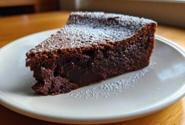 A decadent slice of flourless chocolate torte, dusted lightly with powdered sugar, served on a white plate.