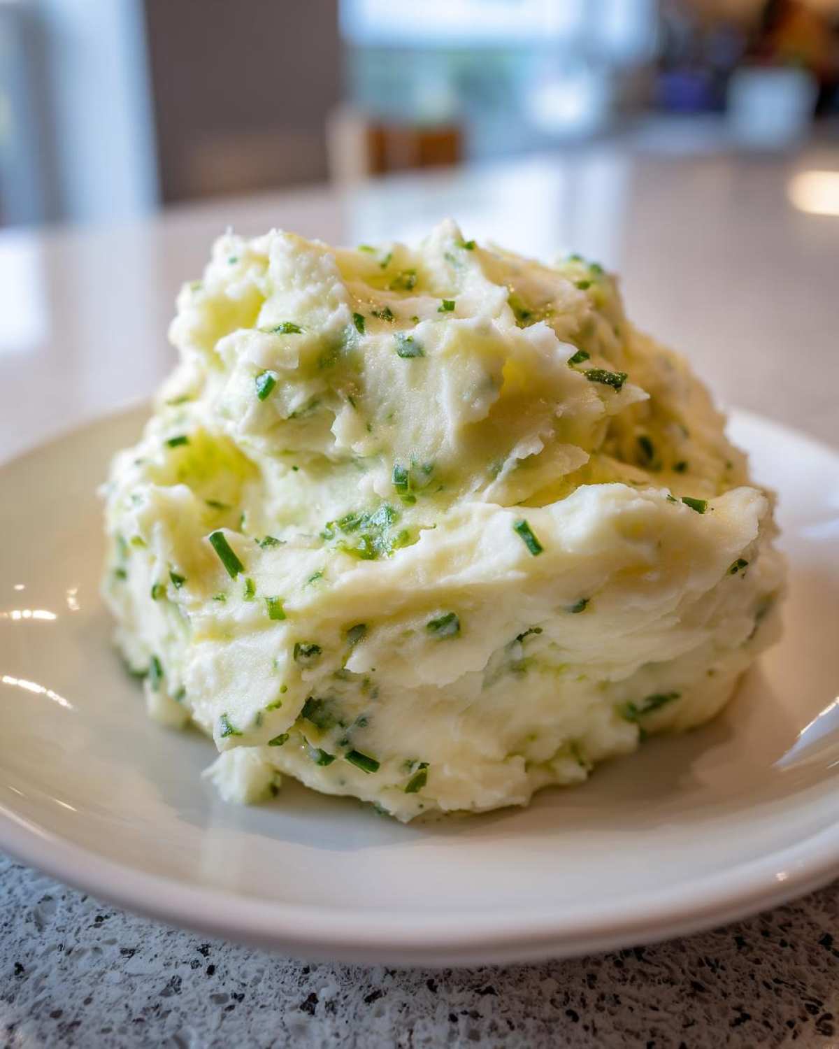 A generous serving of creamy Boursin mashed potatoes mixed with chopped green chives on a white plate.