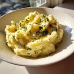 A close-up of a fluffy bowl of garlic mashed potatoes topped with melted butter and fresh chives.