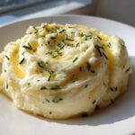 A serving of fluffy garlic mashed potatoes topped with melted butter and fresh chopped chives.