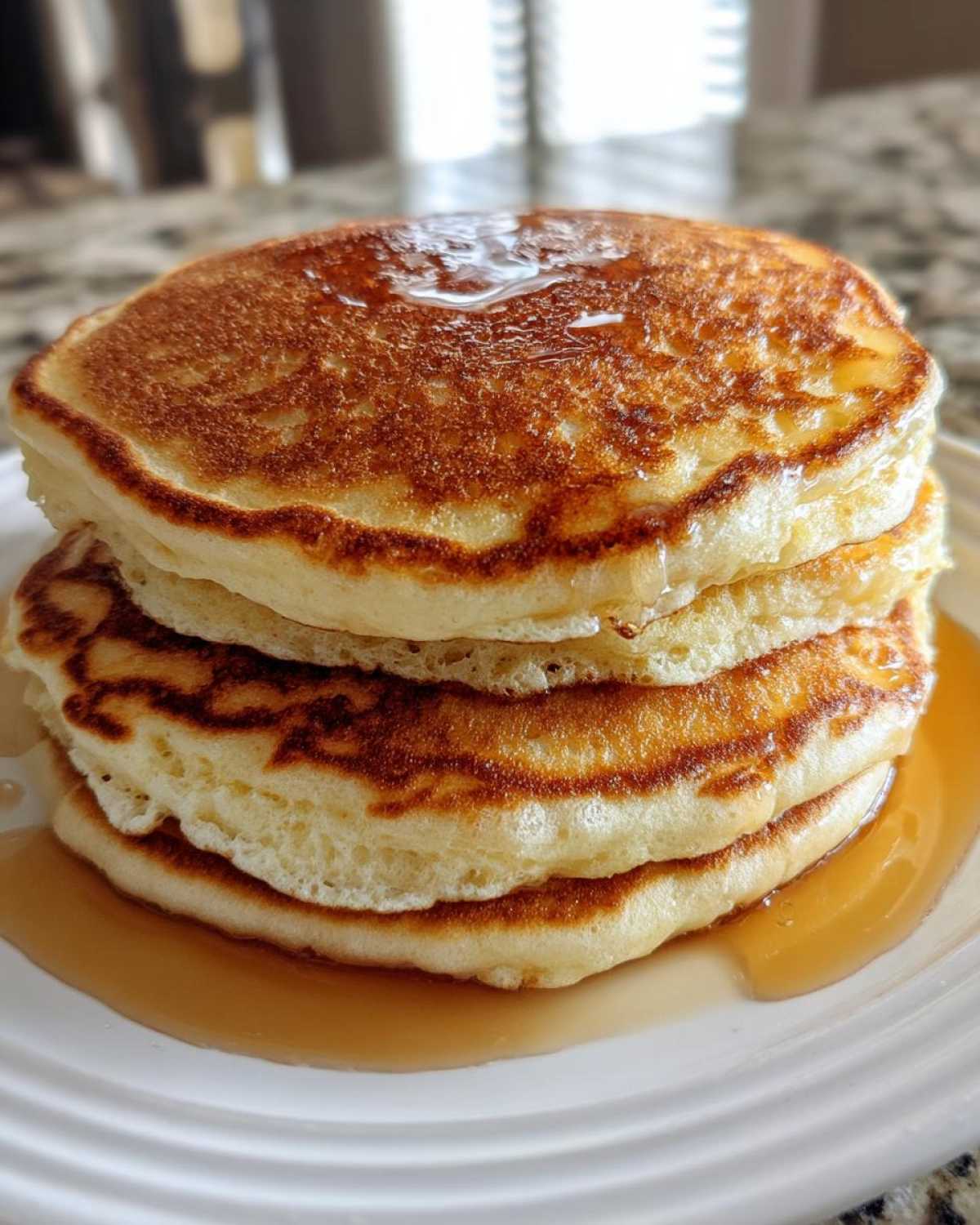 A tall stack of three fluffy pancakes drizzled with golden maple syrup.