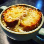 Close-up of a bowl of rich french onion soup recipe topped with melted, browned cheese over a crouton.
