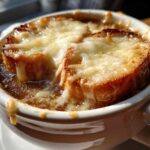 Close-up of a steaming bowl of French onion soup recipe topped with melted Gruyère cheese over toasted bread.