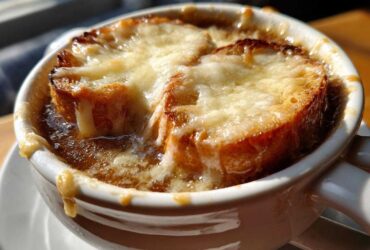 Close-up of a steaming bowl of French onion soup recipe topped with melted Gruyère cheese over toasted bread.