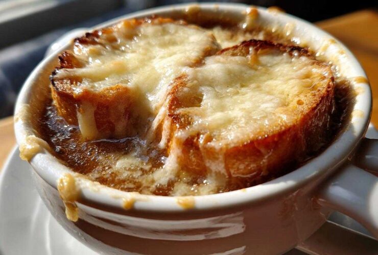 Close-up of a steaming bowl of French onion soup recipe topped with melted Gruyère cheese over toasted bread.