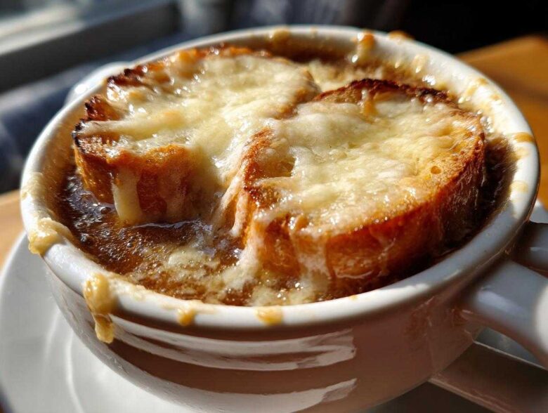 Close-up of a steaming bowl of French onion soup recipe topped with melted Gruyère cheese over toasted bread.