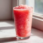 Close-up of a tall glass filled with a bright red, icy strawberry daiquiri, perfectly blended.