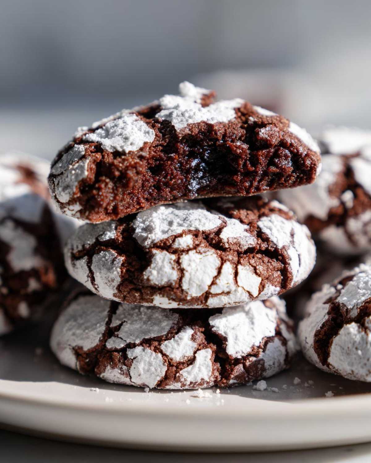 Close-up of a stack of three fudgy crinkle cookies, heavily coated in powdered sugar, with the top cookie broken open.