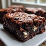 Close-up of a fudgy Oreo brownie square showing chunks of white filling and a shiny, crinkly top.