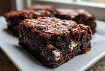 Close-up of a fudgy Oreo brownie square showing chunks of white filling and a shiny, crinkly top.