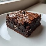 A close-up of a fudgy square of oreo brownies showing the shiny crust and visible cookie pieces inside.