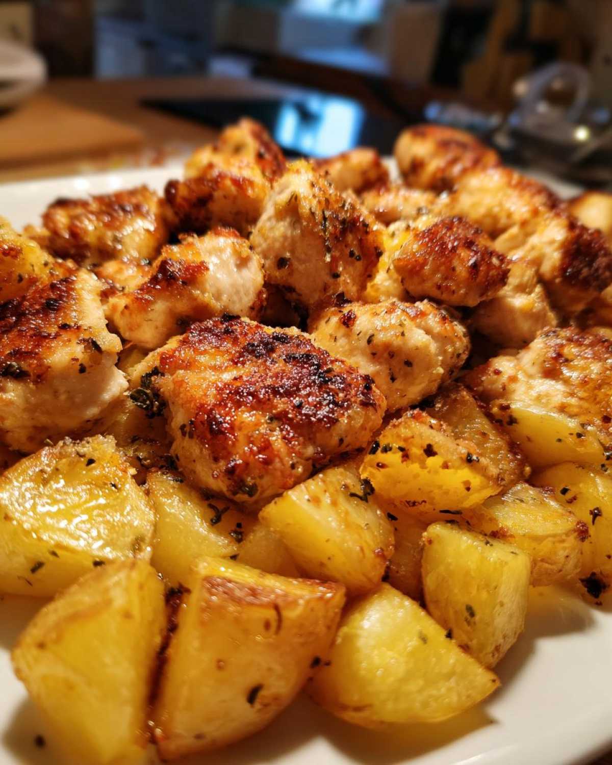 Close-up of golden brown, seasoned chicken pieces served over roasted potatoes, highlighting the garlic parmesan chicken and potatoes.